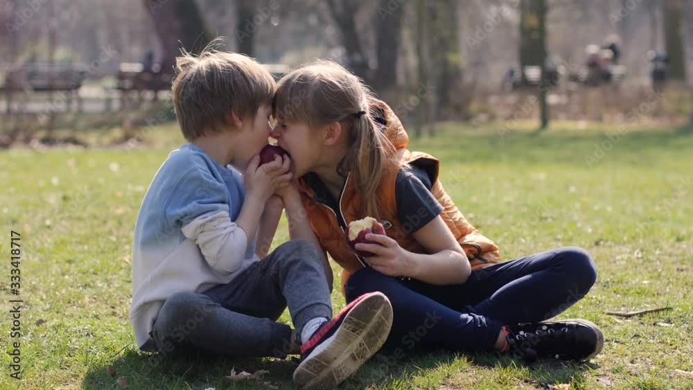 Children brother and sister together funny eat apples fruits sitting on park grass outdoors on daytime Children brother and sister together funny eat apples fruits sitting on park grass outdoors on daytime