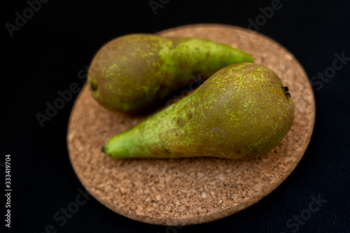 Two green pears laying on cork base on black background