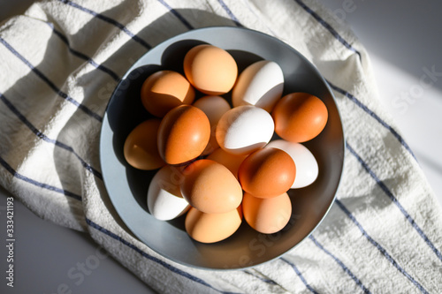 chicken eggs white and brown color in a gray plate on a checked kitchen towel on a white table. concept farm products and natural nutrition. hard sunlight and shadows