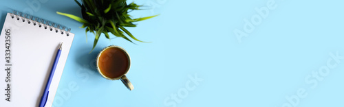 Fotografie notebook or sketchbook and a pen and tea cup and green plant on a blue background