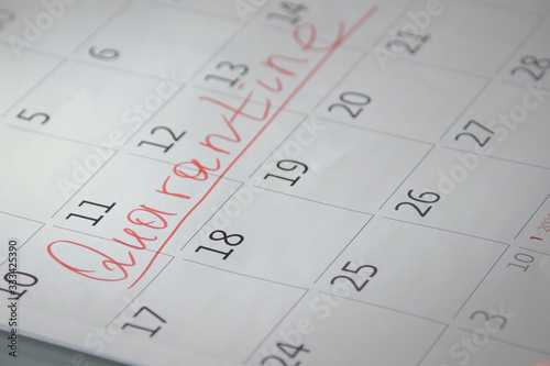 Close-up of unrecognizable person writes Quarantine with a red felt-tip pen on a calendar. Quarantine compliance. Calendar showing nothing to do except quarantine when pandemic covid-19 is raging