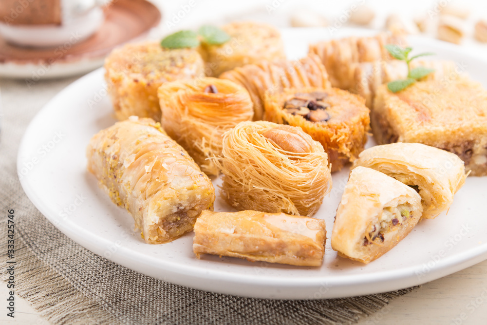 traditional arabic sweets (kunafa, baklava) and a cup of coffee on a white wooden background. side view, selective focus. traditional arabic sweets (kunafa, baklava) and a cup of coffee on a white wooden background. side view, selective focus.