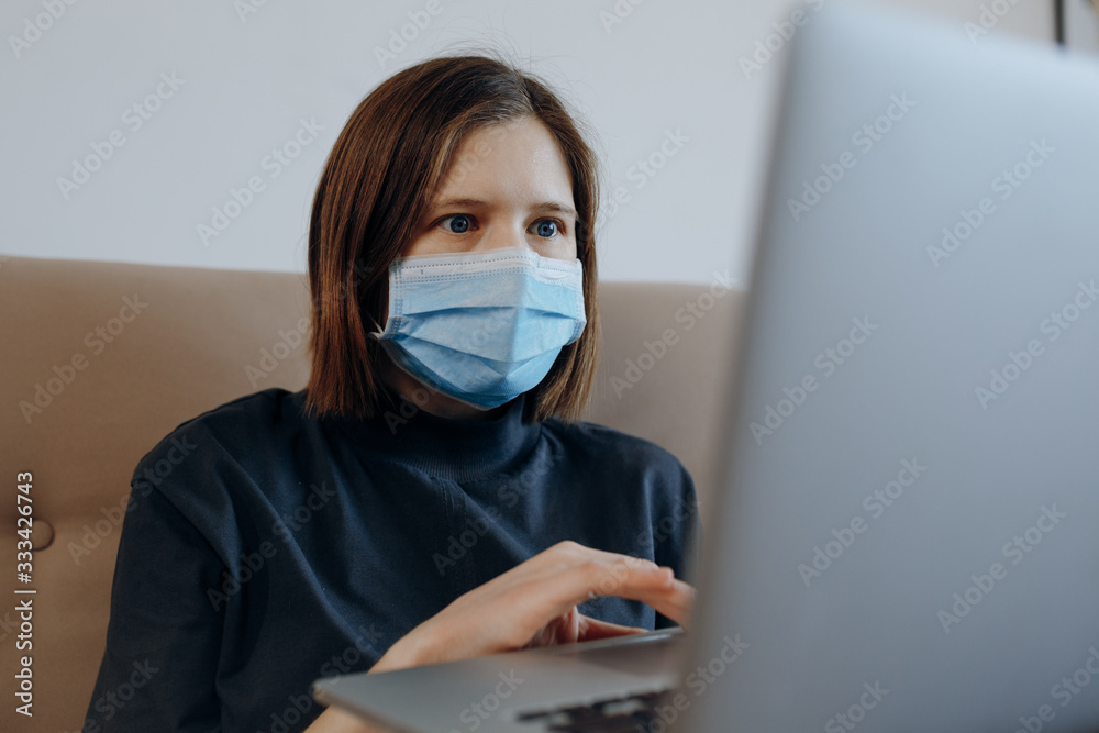 World pandemic. Woman with protective mask on her face isolating at home, reading last news about coronavirus from laptop. Shock face. Social distancing, stay home concept. 
