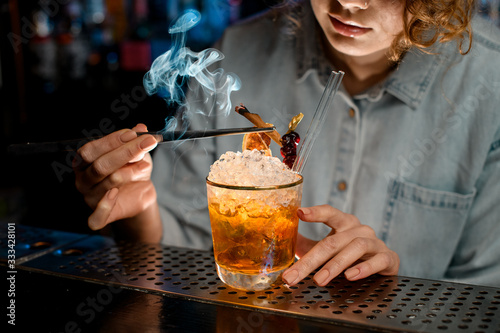 Close-up. Woman bartender decorates glass with cocktail by smoking stick
