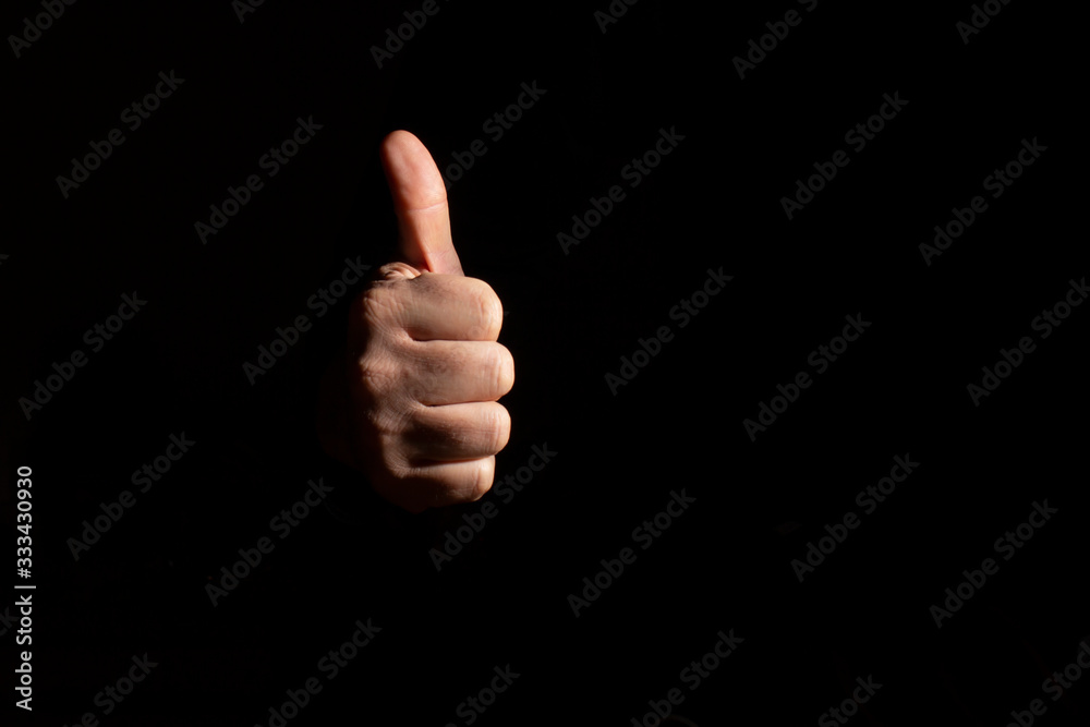Hand of a man with thumb up. Well being, luck and joy concept. Black color background. Free space to write.