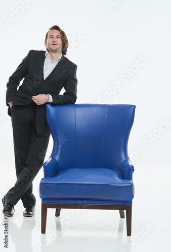 The handsome men in black suit is at blue leather chair, white background, brutal man with long hairs, white shirts, business man, very stylish