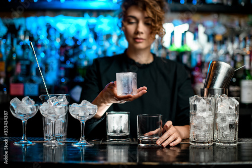 young bartender woman holds in hand large piece of ice.