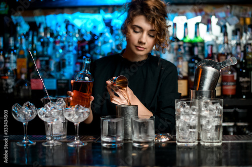 bartender lady pours drink into metal glass using jigger