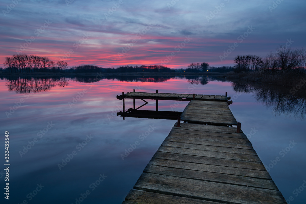 Wooden fishing pier on the lake and colorful clouds after sunset