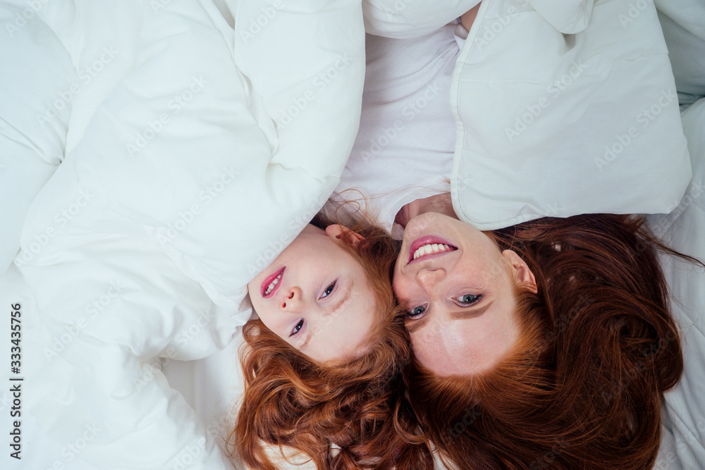two happy redhaired ginger girls playing hide and seek under white blanket