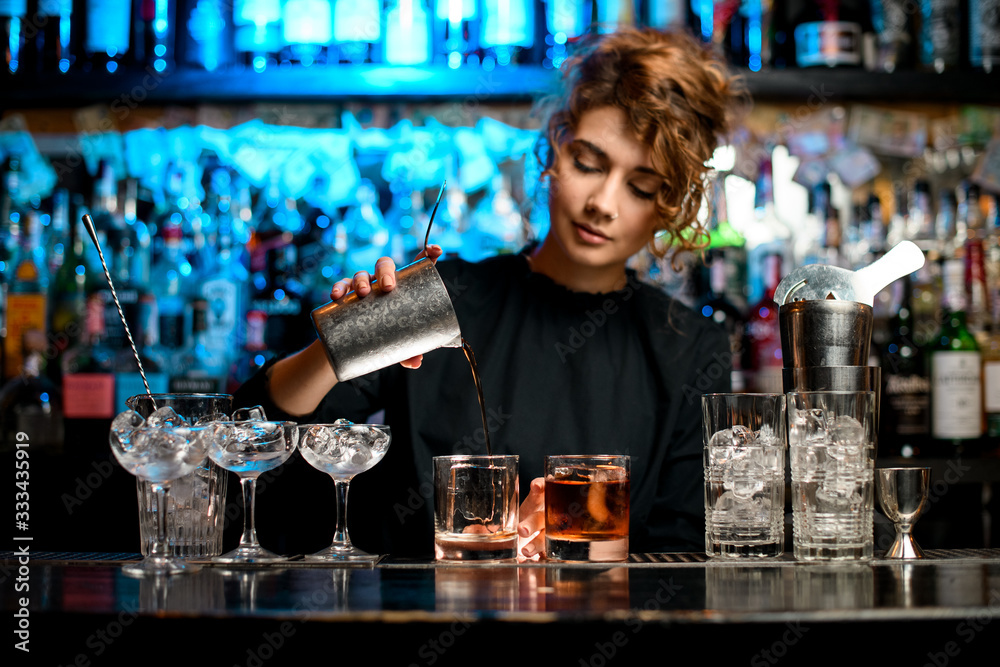 Young woman barman preparing cocktail and pouring it into glass. - obrazy, fototapety, plakaty 