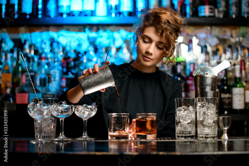Young woman barman preparing cocktail and pouring it into glass. photo