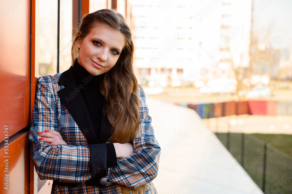 Portrait of a pretty beautiful young girl with long hair with a smile in the park against the background of a building wall. Photo taken in sunny weather outdoors in spring. Portrait of a pretty beautiful young girl with long hair with a smile in the park against the background of a building wall. Photo taken in sunny weather outdoors in spring.