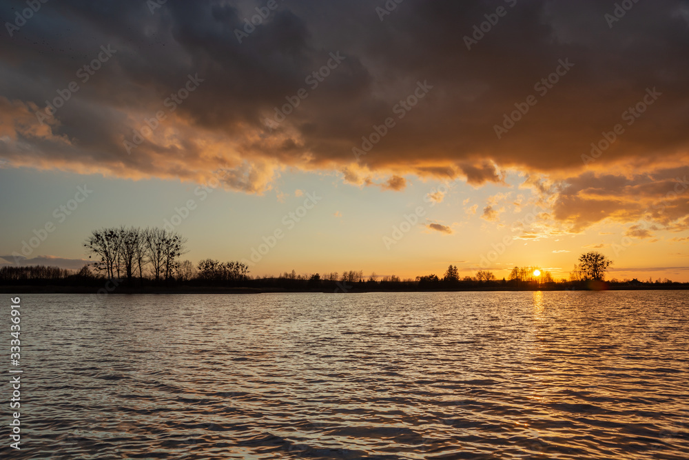 Dark cloud over the lake, trees on the horizon and sunset