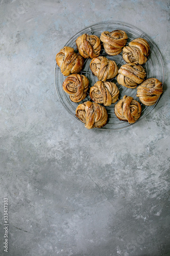 Traditional Swedish cardamom sweet buns Kanelbulle on cooling rack over grey concrete texture background. Flat lay, space photo