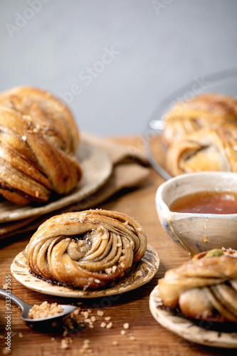 Traditional Swedish cardamom sweet buns Kanelbulle on plate, ingredients in ceramic bowl above on wooden table. photo