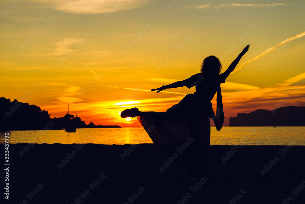 Silhouette of dancing young woman on the beach near sea during sunset. Holidays and enjoying life concept