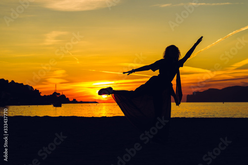 Silhouette of dancing young woman on the beach near sea during sunset. Holidays and enjoying life concept