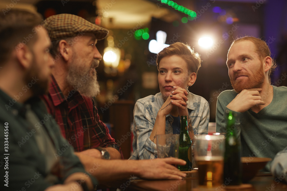 Group of people talking to each other while sitting at the table with beer and alcohol drinks in the pub