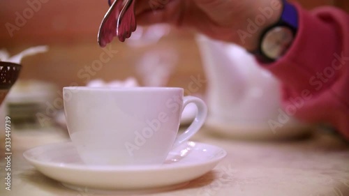 Close up of woman's hands putting piece of suger into bowl of tea. Tea drinking ceremony.