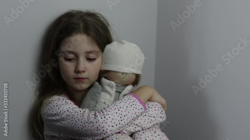 little girl with a doll is sitting in the corner and crying. the violence of their parents, child labour, child abuse