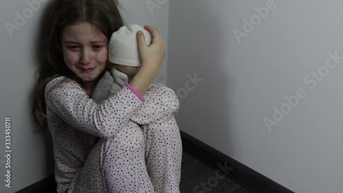 little girl with a doll is sitting in the corner and crying. the violence of their parents, child labour, child abuse