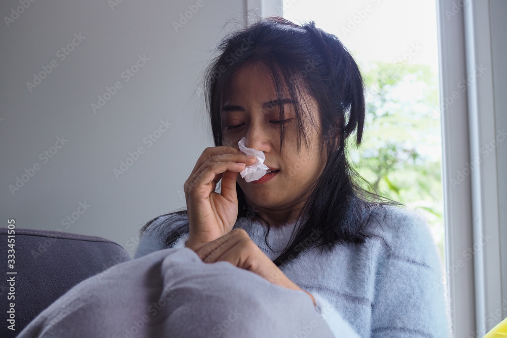 Asian woman is sick having stuffy nose, flowing water in the hands, wiping paper, high fever Sitting on the sofa inside the house Asian woman is sick having stuffy nose, flowing water in the hands, wiping paper, high fever Sitting on the sofa inside the house