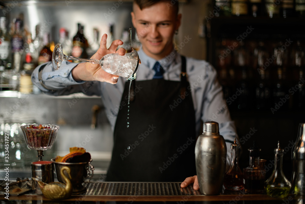 bartender holds wineglass with ice and pours liquid from it.