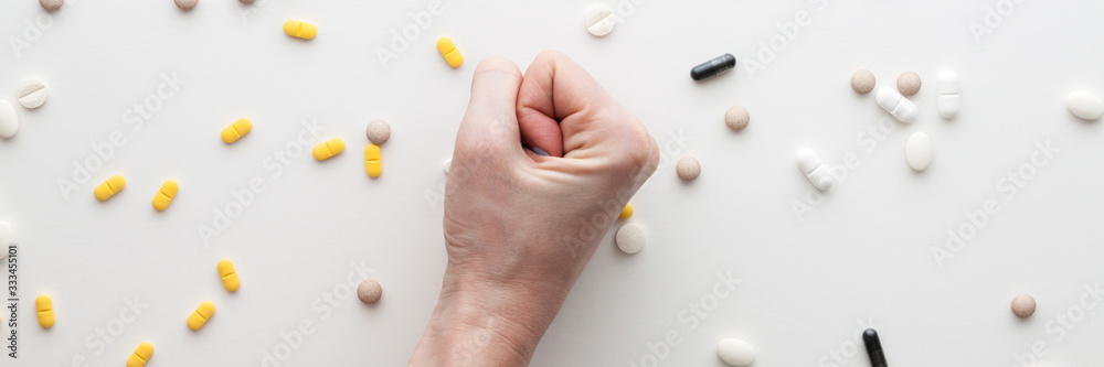 White background with scattered tablets. A clenched female hand. Medical background. Fighting the epidemic. Panorama White background with scattered tablets. A clenched female hand. Medical background. Fighting the epidemic. Panorama