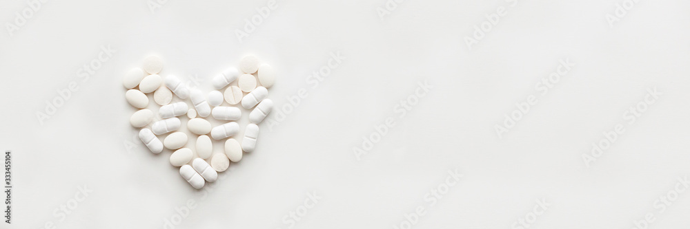 White background with scattered tablets in the shape of a heart. Medical background. Minimal composition. Panorama. Copy space White background with scattered tablets in the shape of a heart. Medical background. Minimal composition. Panorama. Copy space