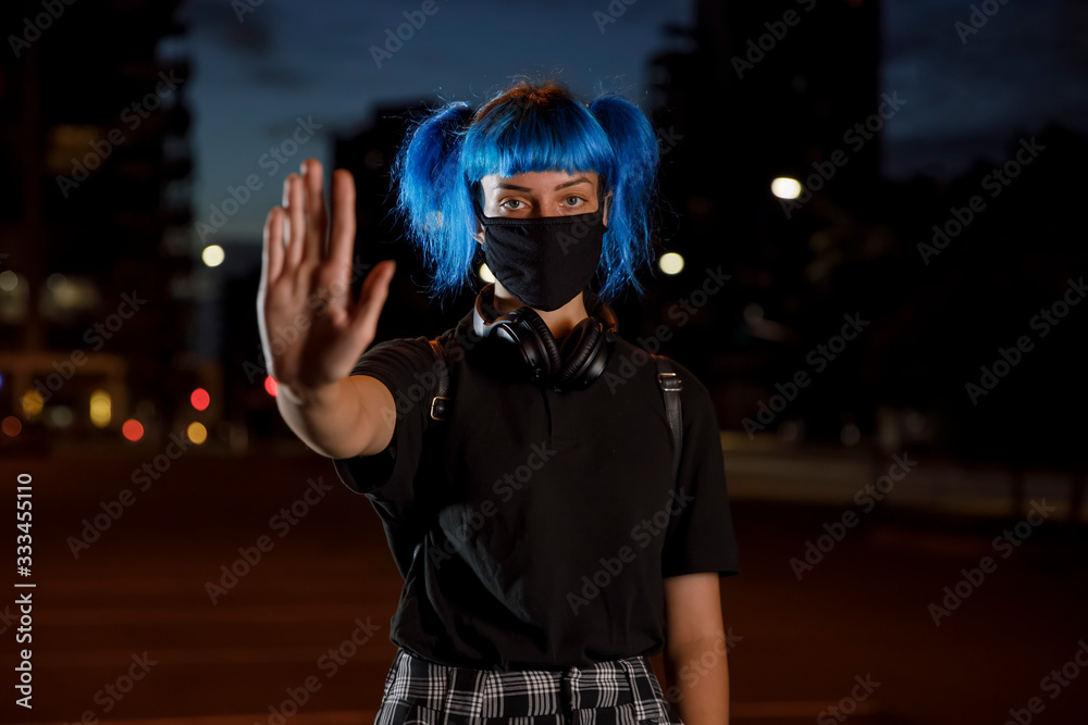 stop coronavirus social distancing concept, young female with blue hair wearing a fashion protective medical face mask, hand and palm up stop gesture, urban city street on dusk, stop covid 19 pandemic stop coronavirus social distancing concept, young female with blue hair wearing a fashion protective medical face mask, hand and palm up stop gesture, urban city street on dusk, stop covid 19 pandemic
