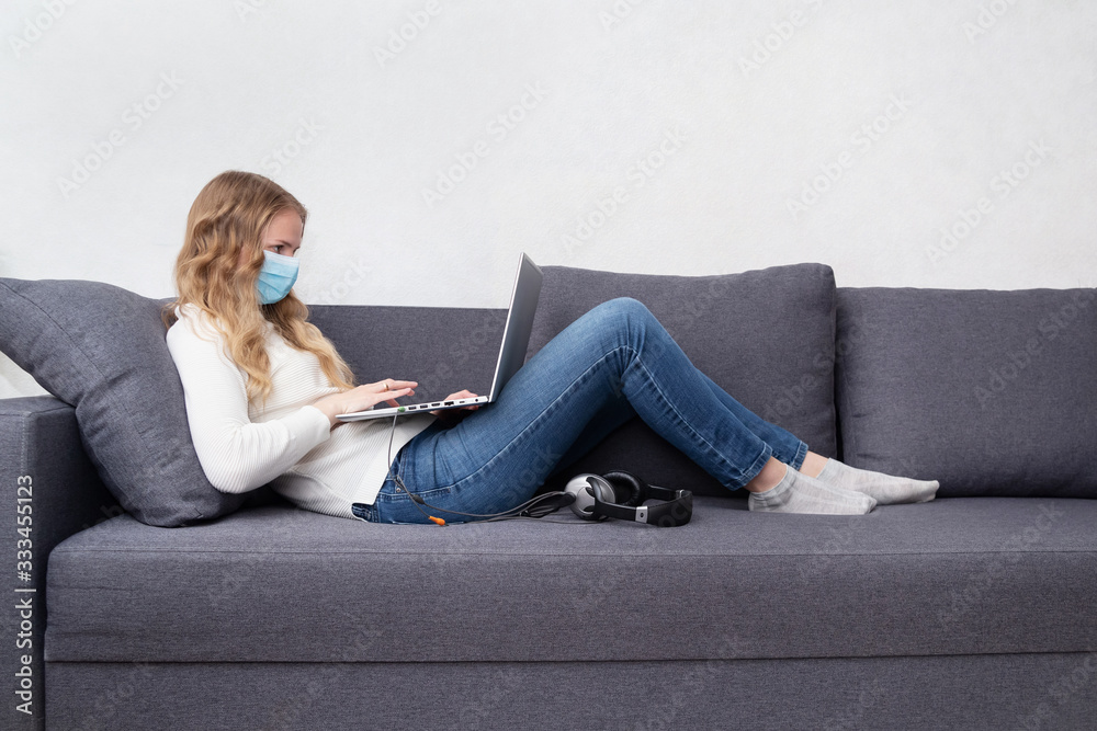 Woman in a respiratory mask working home sitting on a sofa with a laptop. Stay home, quarantine concept Woman in a respiratory mask working home sitting on a sofa with a laptop. Stay home, quarantine concept