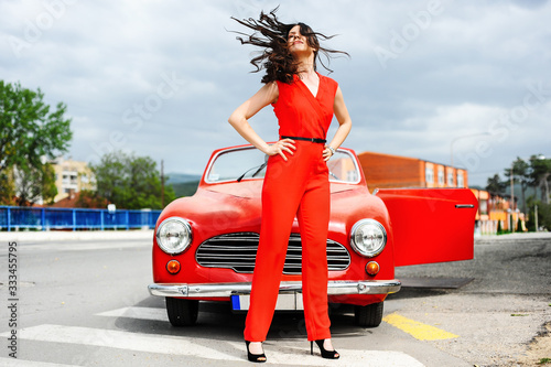 Pretty Young woman standing in front of the red car old timer cabriolet on the road in summer day vacation road trip wind in hair