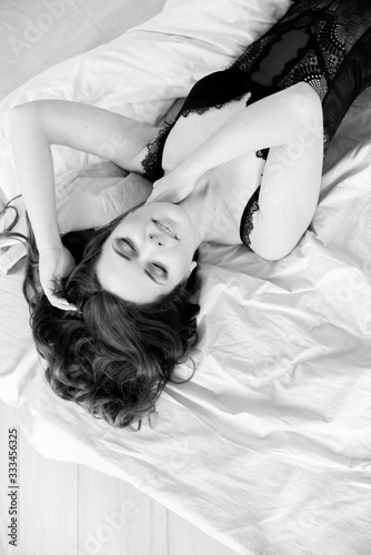 Young attractive woman with long curly hair in jeans and a lace black t-shirt on the bed in the bedroom