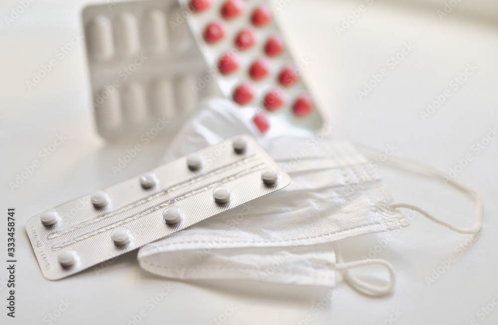 medical face mask and many different pills in blisters. Photo on a white background with bokeh. medical face mask and many different pills in blisters. Photo on a white background with bokeh.