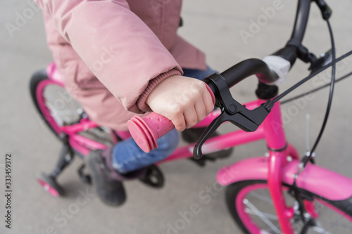 The child is holding the wheel of a bicycle. A girl in a pink jacket is riding her bike