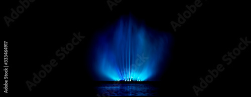 Night show of fountains. Blue spray of water on a black background. Banner.