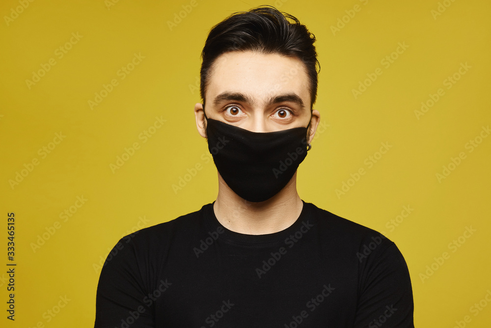 Handsome man in black t-shirt and black protective mask isolated on yellow background. Healthy lifestyle concept, seasonal illness, and seasonal flu concept. Handsome man in black t-shirt and black protective mask isolated on yellow background. Healthy lifestyle concept, seasonal illness, and seasonal flu concept.
