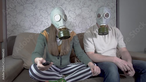 Daughter and father in gas masks sit on the couch in the room. They watch TV during the epidemic. The concept of Personal safety in an infectious pandemic or the threat of radioactive contamination photo