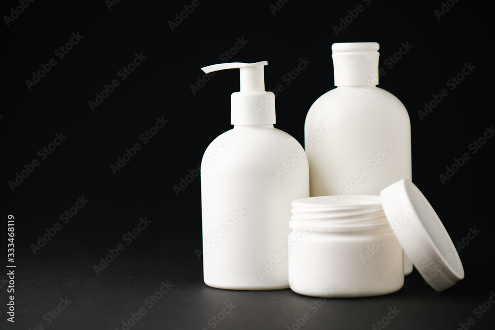 container with face cream near white bottles on black container with face cream near white bottles on black