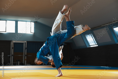 Two young judo caucasian fighters in white and blue kimono with black belts training martial arts in the gym with expression, in action, motion. Practicing fighting skills. Overcoming, reaching target photo