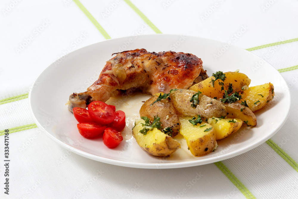 Roasted chicken leg with roasted potatoes and parsley on a white plate, topped with tomato salad