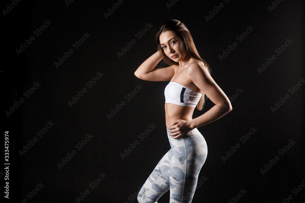 Portrait of young beautiful sportive girl posing over dark background.