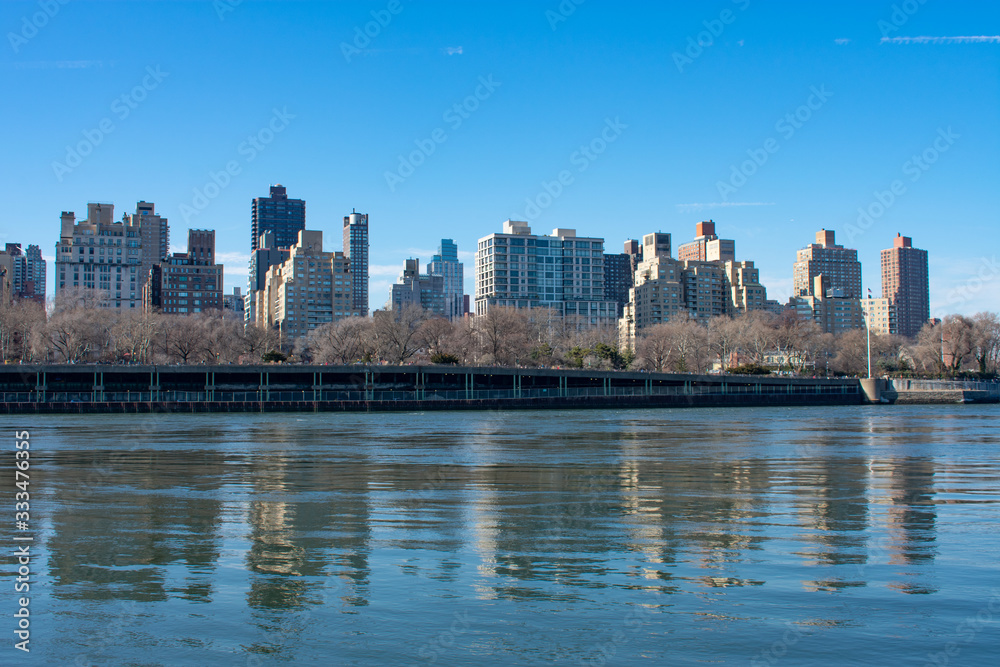 Naklejka premium Upper East Side New York City Skyline along the East River with a Clear Blue Sky and Reflections