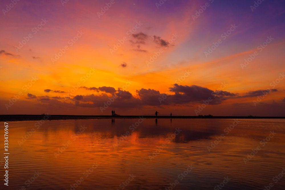 Burning bright sky during sunset on a tropical beach. Sunset during the exodus, the strength of people walking on water Burning bright sky during sunset on a tropical beach. Sunset during the exodus, the strength of people walking on water
