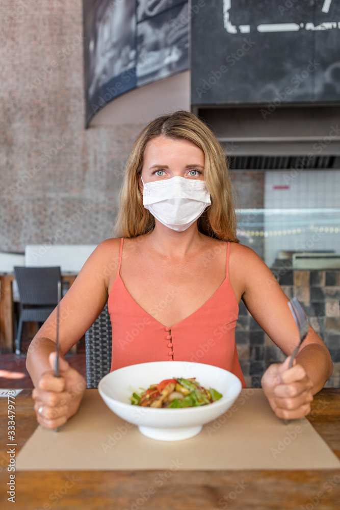 A woman in a protective surgical mask on her face, sitting at a table in a restaurant. Chinese coronavirus disease COVID-19 is a dangerous virus.Pandemic.