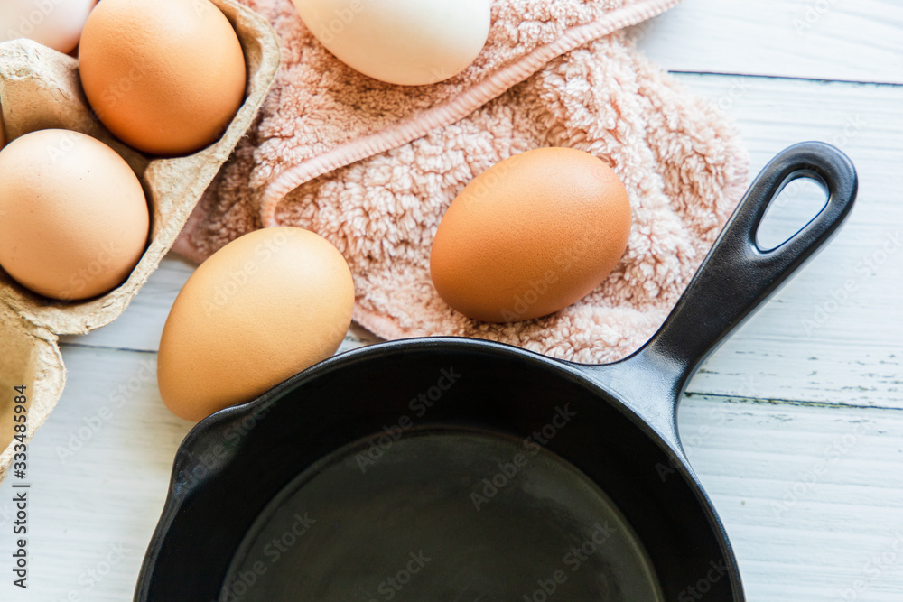 Organic chicken eggs in brown paper boxes and black pans placed on a white wooden table Breakfast ingredients Organic chicken eggs in brown paper boxes and black pans placed on a white wooden table Breakfast ingredients