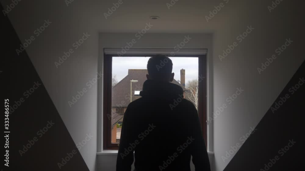 Young male adult self isolating in house, walking to window looking outside