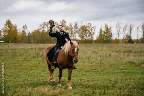 The concept of falconry. A man with a leather glove and a beautiful Falcon on handon a chestnut, red, and red horse