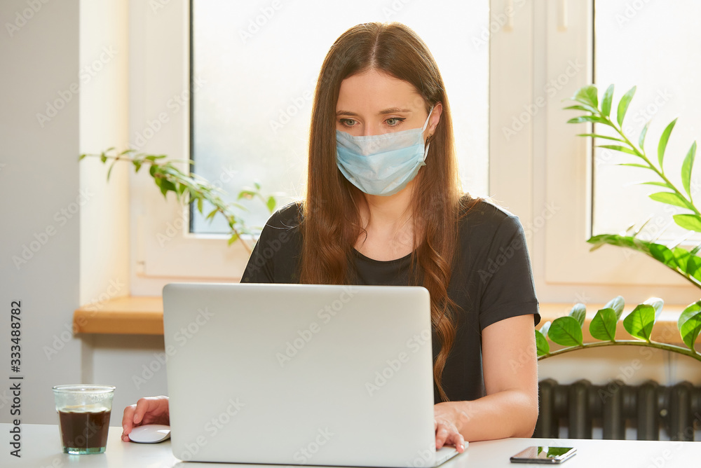 A caucasian woman in a medical face mask working remotely on her laptop during the quarantine to avoid the spread coronavirus. A businesswoman working from home during the pandemic of COVID-19. A caucasian woman in a medical face mask working remotely on her laptop during the quarantine to avoid the spread coronavirus. A businesswoman working from home during the pandemic of COVID-19.